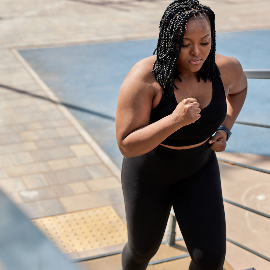 Obese young african woman foing fitness exercises on stairs outdoors. Weight loss cardio goal achievement challenge. Copy space. Side view portrait of black lady in black tracksuit engaged in fitness