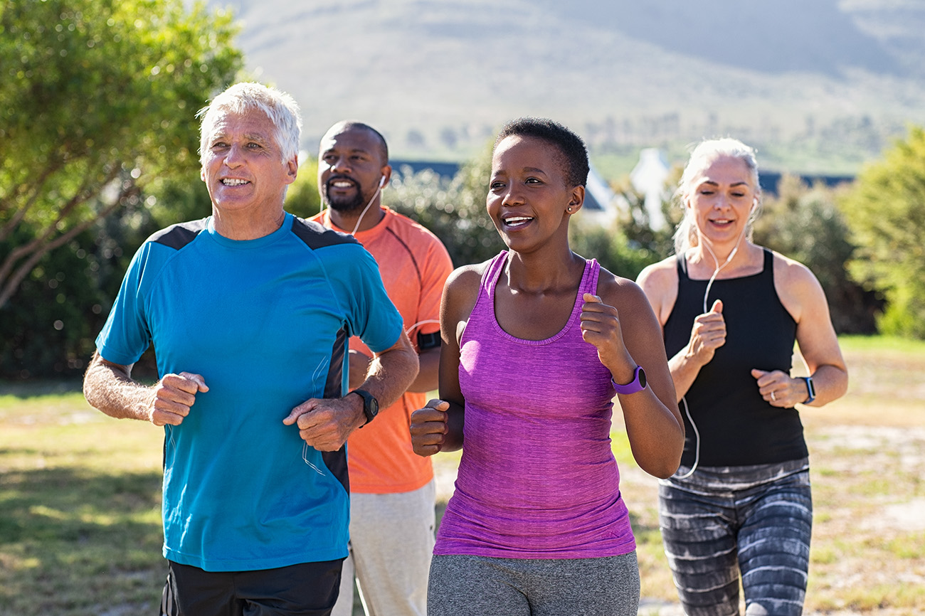 Healthy group of mature people jogging on track at park. Happy senior couple running at park with african friends. Multiethnic middle aged friends exercising together outdoor.